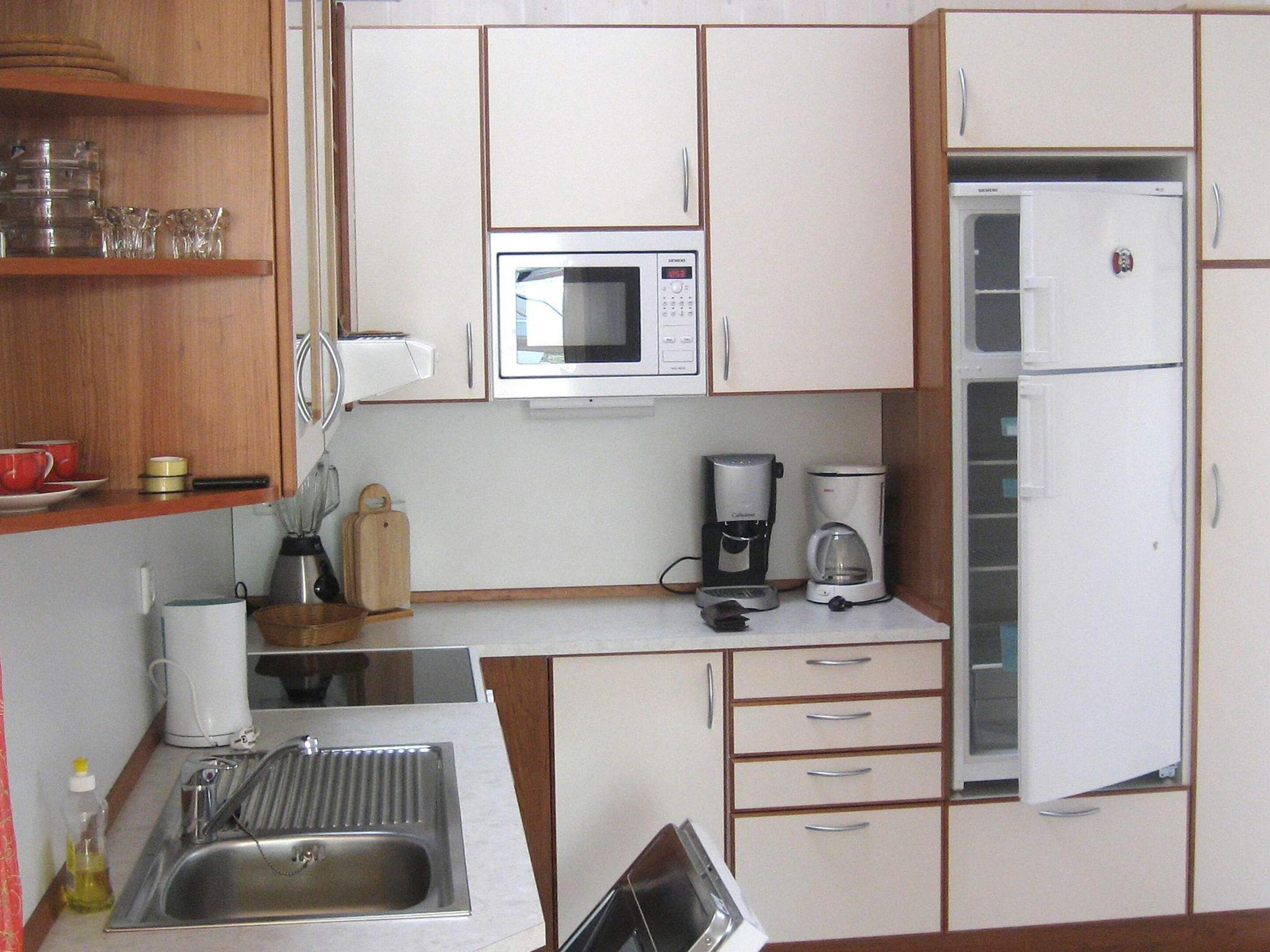 A compact kitchen with a microwave, coffee maker, refrigerator, and a sink.