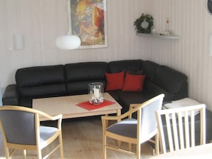 A living room with a black sofa, two wooden chairs, a small table with a glass candle holder, and a painting on the wall.