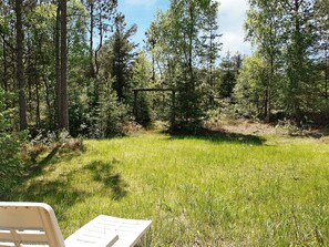 A grassy outdoor area with a wooden swing set, surrounded by tall trees.
