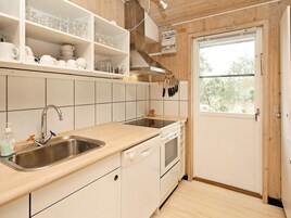 Una cocina con un lavamanos, encimera y armarios. Se ve una ventana con vista a árboles.
