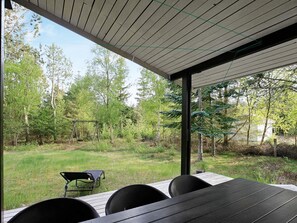 An outdoor seating area with a table and chairs, overlooking a grassy yard with trees and a swing set. - 8 Person Holiday Home in Albaek (Jerup)