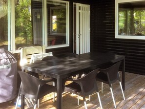 An outdoor dining area with a wooden table and chairs, a barbecue grill, and a sliding glass door leading to a covered patio.