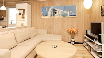 Uma sala de estar moderna com um sofá seccional bege, uma mesa de centro redonda de madeira, uma TV de tela plana em um suporte e uma parede de madeira com uma pintura grande.