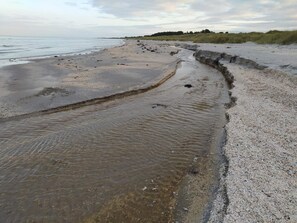 Une plage séparée de la mer par un étroit chenal d’eau.