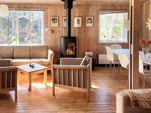 A cozy cabin interior with a wooden interior, a fireplace, a sofa, a dining table, and chairs.
