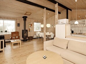 A modern interior with a wooden floor, a sofa, a dining table with chairs, a kitchen area, and a fireplace.