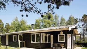 En stuga med en veranda, stora fönster och en skorsten.