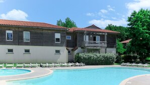 Una piscina con sillones de descanso, un edificio de madera con balcón y un cielo azul despejado.