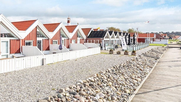 A row of red-roofed, white-framed beach houses with a gravel path and wooden boardwalk.