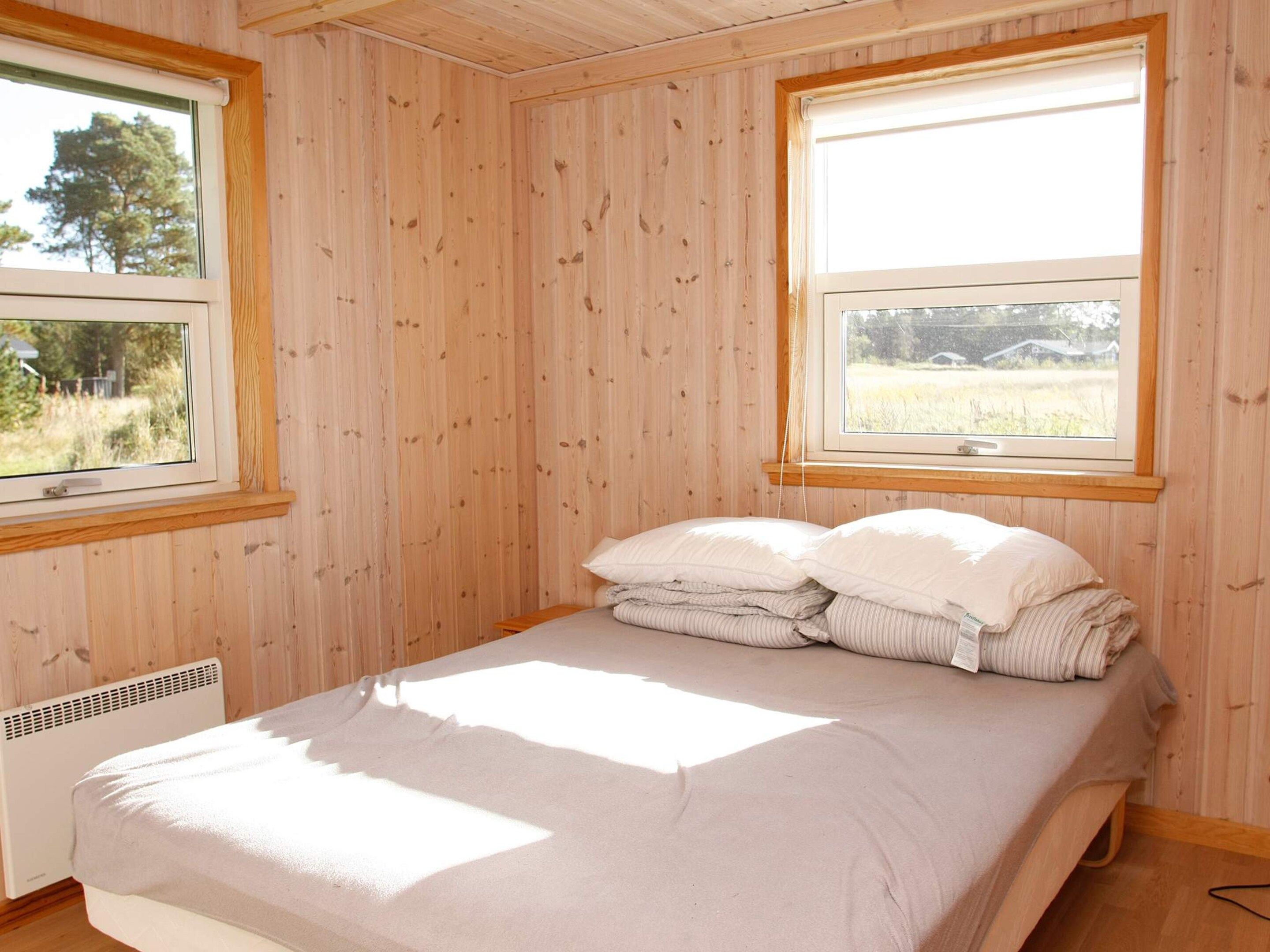 A single bed with a white mattress and pillows, a window with a view of a field, and wooden panel walls.