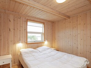 A room with a wooden ceiling, a single bed with white bedding, a bedside table, and a window with a view of greenery. - 8 Person Holiday Home in Jerup (Jerup)