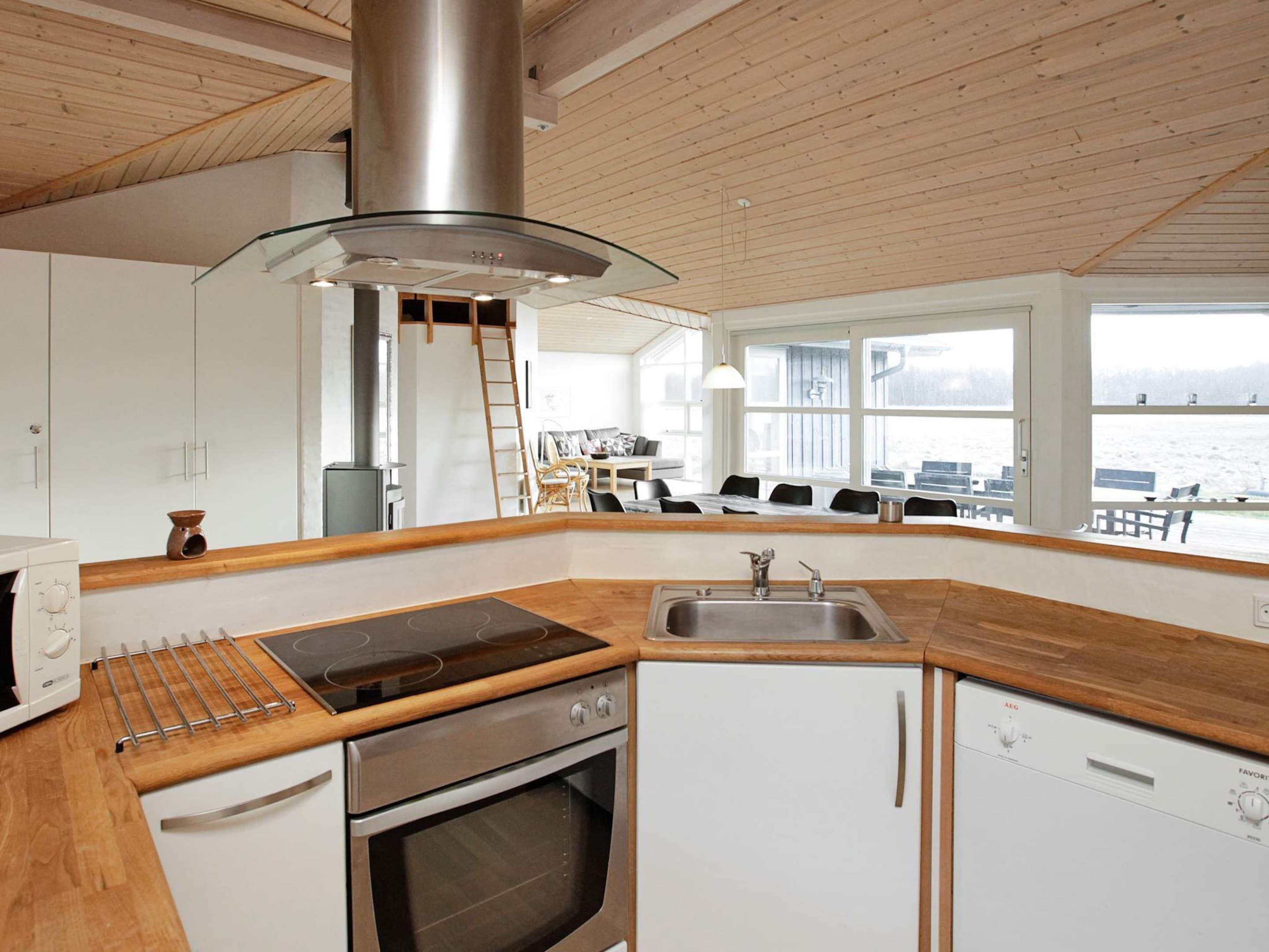 A modern kitchen with a stove, oven, and sink, wooden countertops, and a view of the sea through large windows.