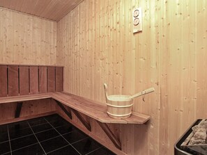 A sauna room with wooden walls, a bench, a bucket, and a heater. - 8 Person Holiday Home in Jerup (Jerup)