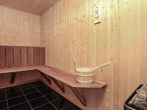 Et sauna-rum med trævægge, en bænk, en spand og en ovn.