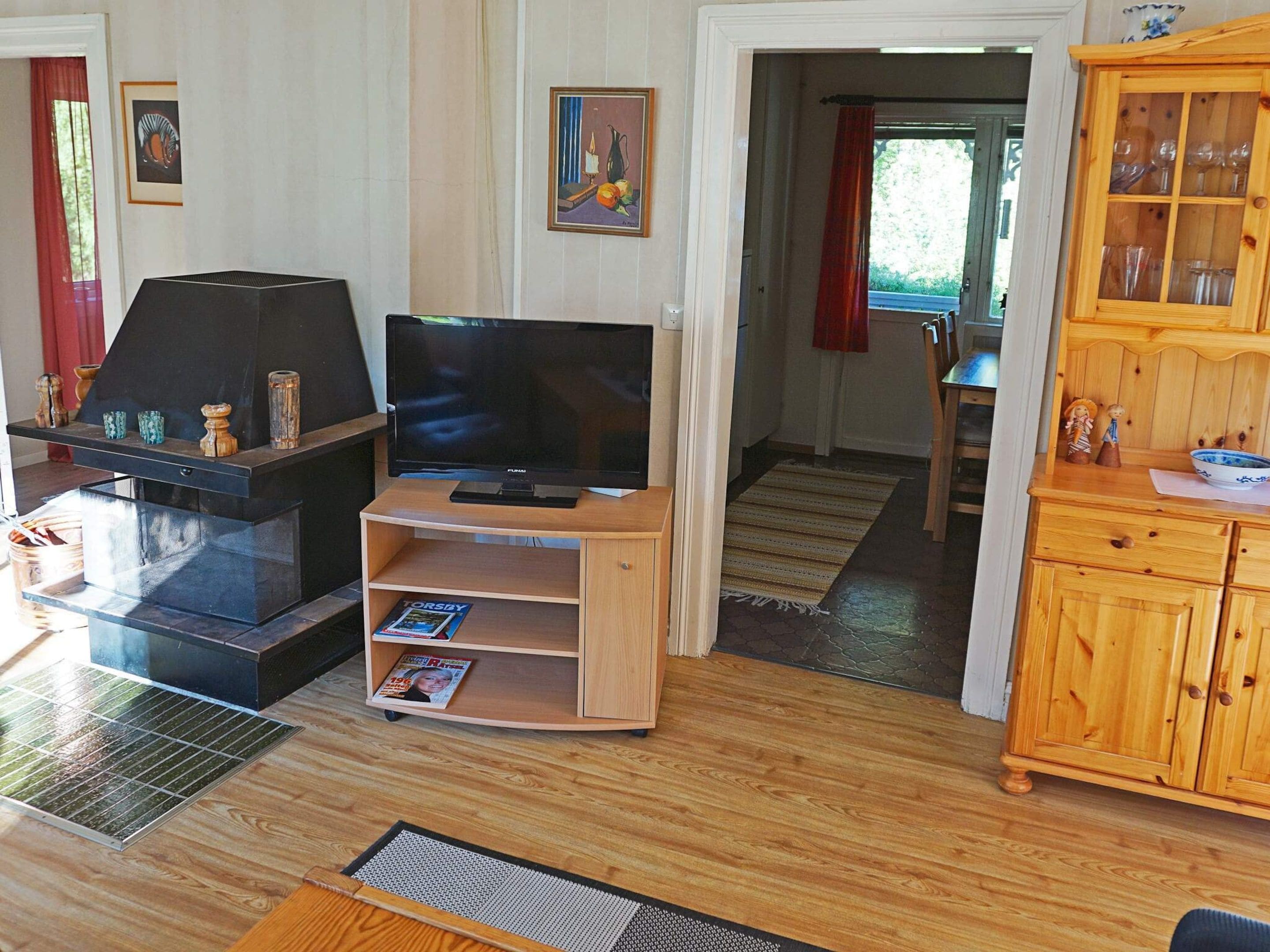 A living room with a TV, fireplace, wooden cabinet, and a dining area visible through an open doorway.