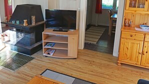 A living room with a TV, fireplace, wooden cabinet, and a dining area visible through an open doorway. - 6 Person Holiday Home in Torsby (Torsby)