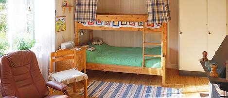 A bunk bed with a green mattress, a wooden desk, a brown leather chair, and a window with curtains.