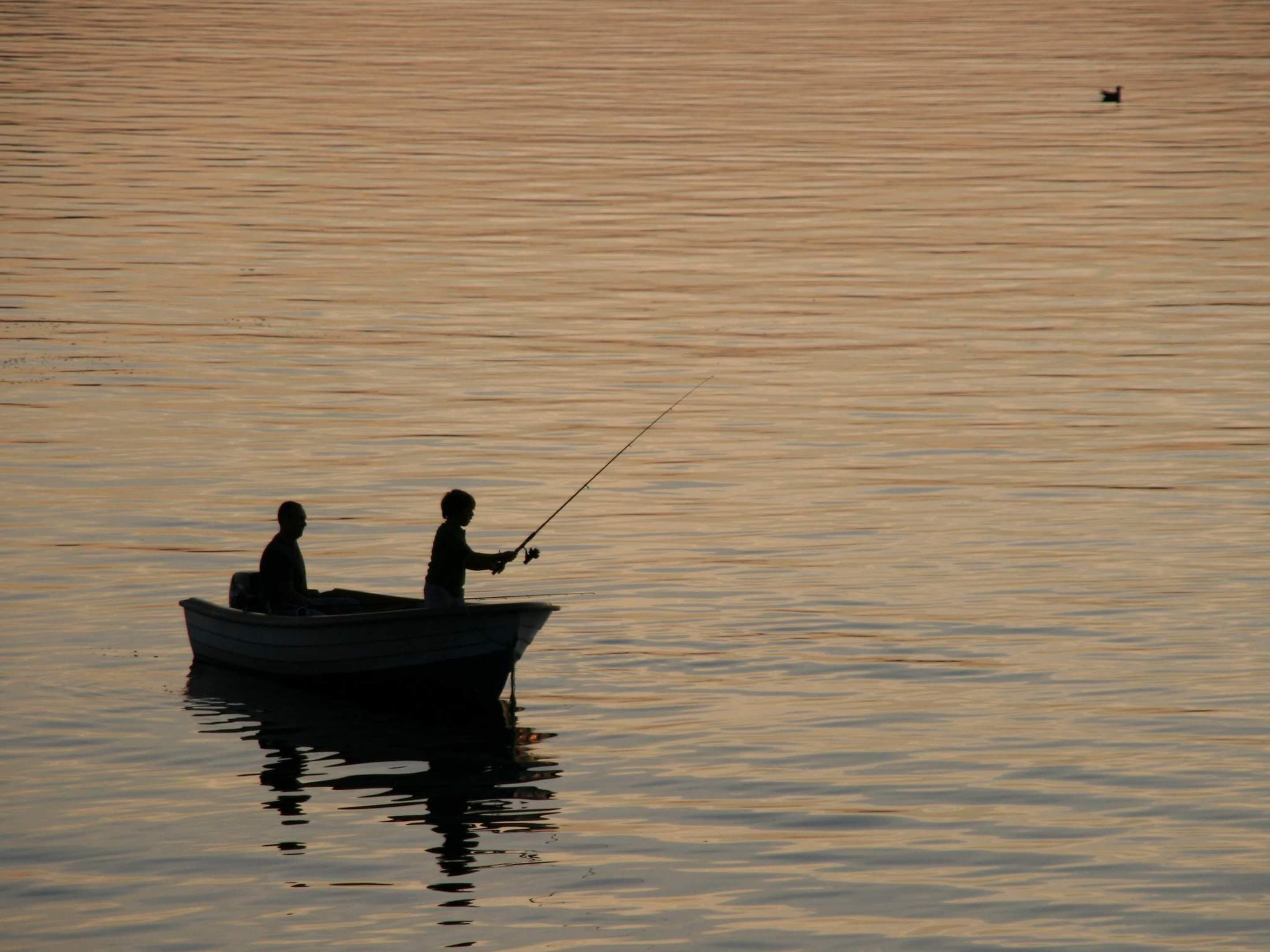 A boat on calm water with two people fishing.