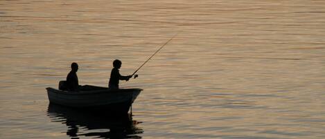 A boat on calm water with two people fishing.