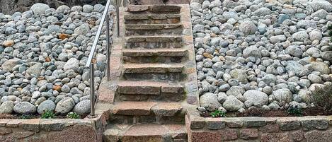 A stone staircase leading up to a rocky area with a metal railing.