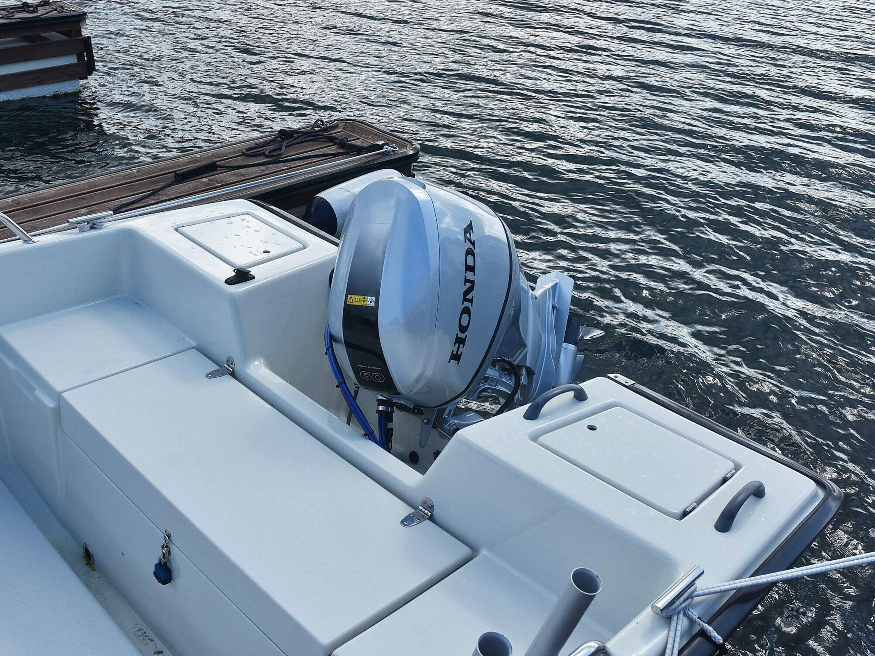 A boat's interior with a Honda outboard motor, a white cushioned seating area, and a wooden dock in the background.