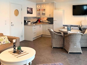 A compact living space with a kitchenette, a sofa, a round coffee table, and wicker chairs. - 5 Star Holiday Home in Urangsvag (Bomlo)