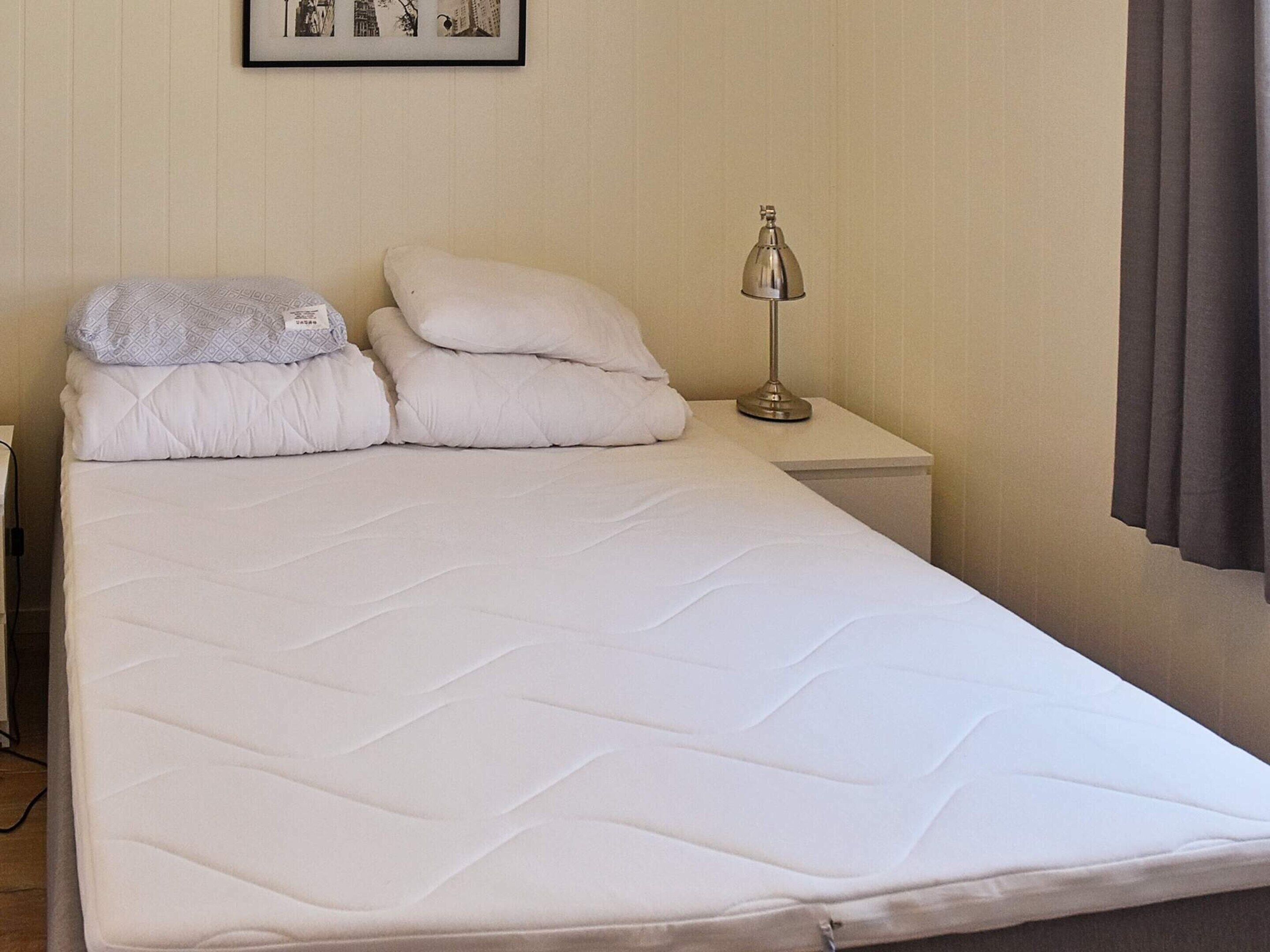 A neatly made bed with white bedding and two pillows, a bedside lamp, and a framed picture on the wall.