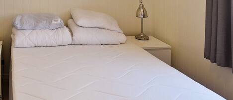 A neatly made bed with white bedding and two pillows, a bedside lamp, and a framed picture on the wall.
