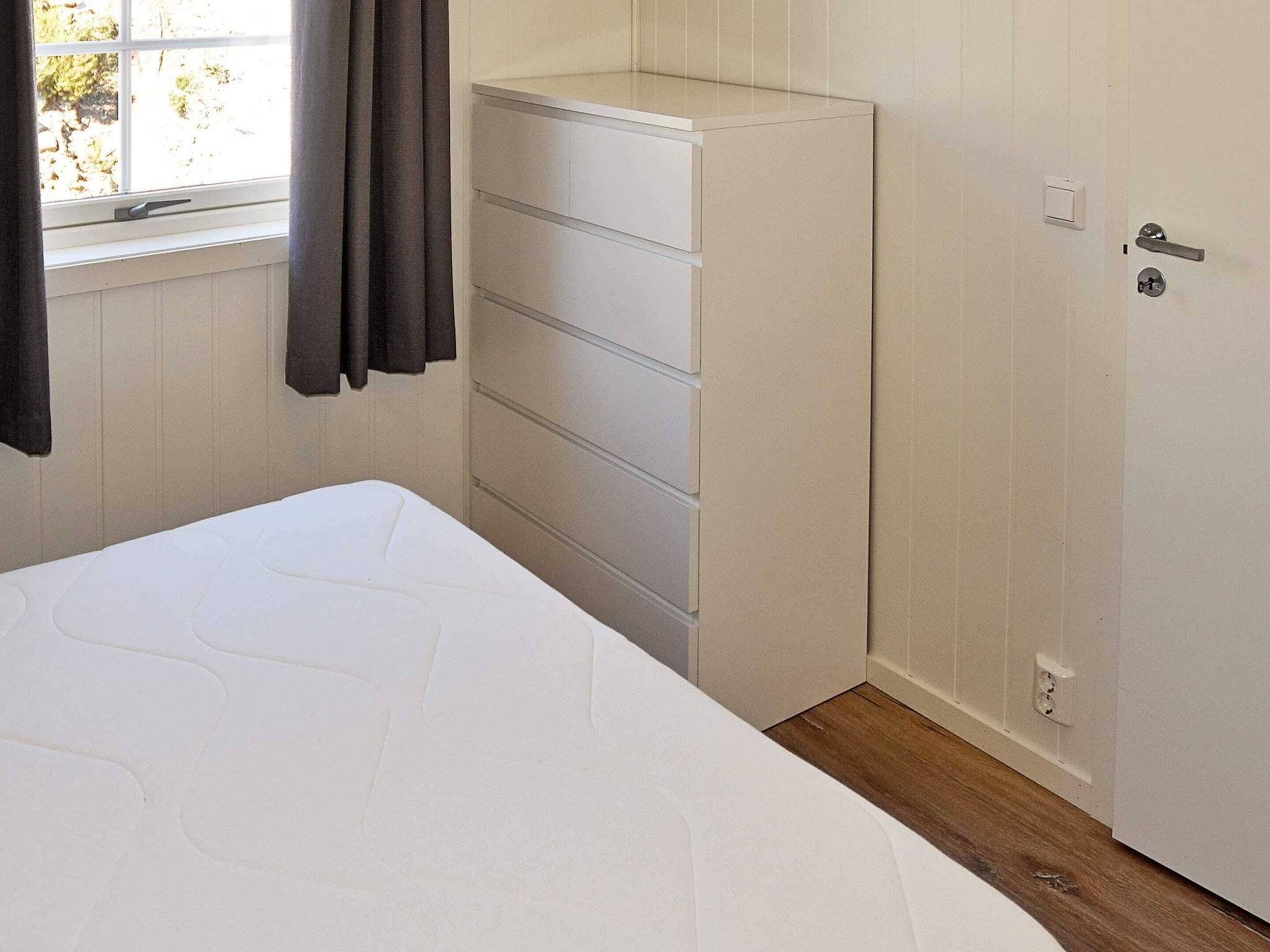 Un dormitorio con cama, cómoda blanca, puerta y ventana con cortinas.
