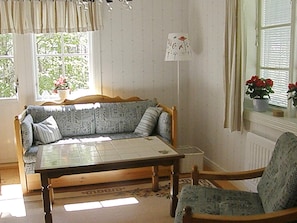 A room with a wooden sofa, a wooden table, a chair, a window with curtains, and a radiator. - 6 Person Holiday Home in Ostmark (Östmark)