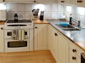 A compact kitchen with a stove, oven, sink, and wooden countertop.