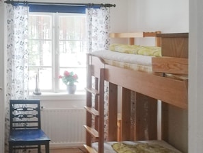 A bunk bed with a wooden frame and a mattress, a chair with a floral pattern, and a window with curtains. - 6 Person Holiday Home in Ostmark (Östmark)