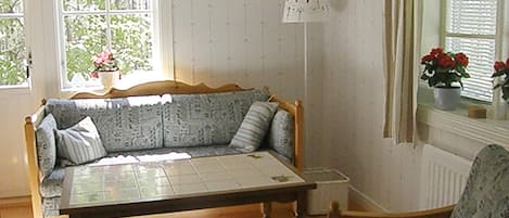 A room with a wooden sofa, a wooden table, a chair, a window with curtains, and a radiator.