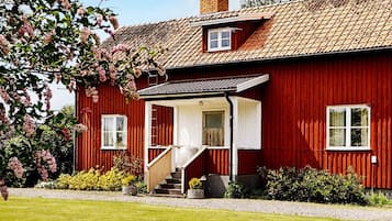 A red wooden house with a white porch, a chimney, and a small window.