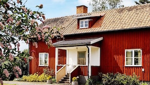Una casa de madera roja con un porche blanco, una chimenea y un ventanal pequeño.