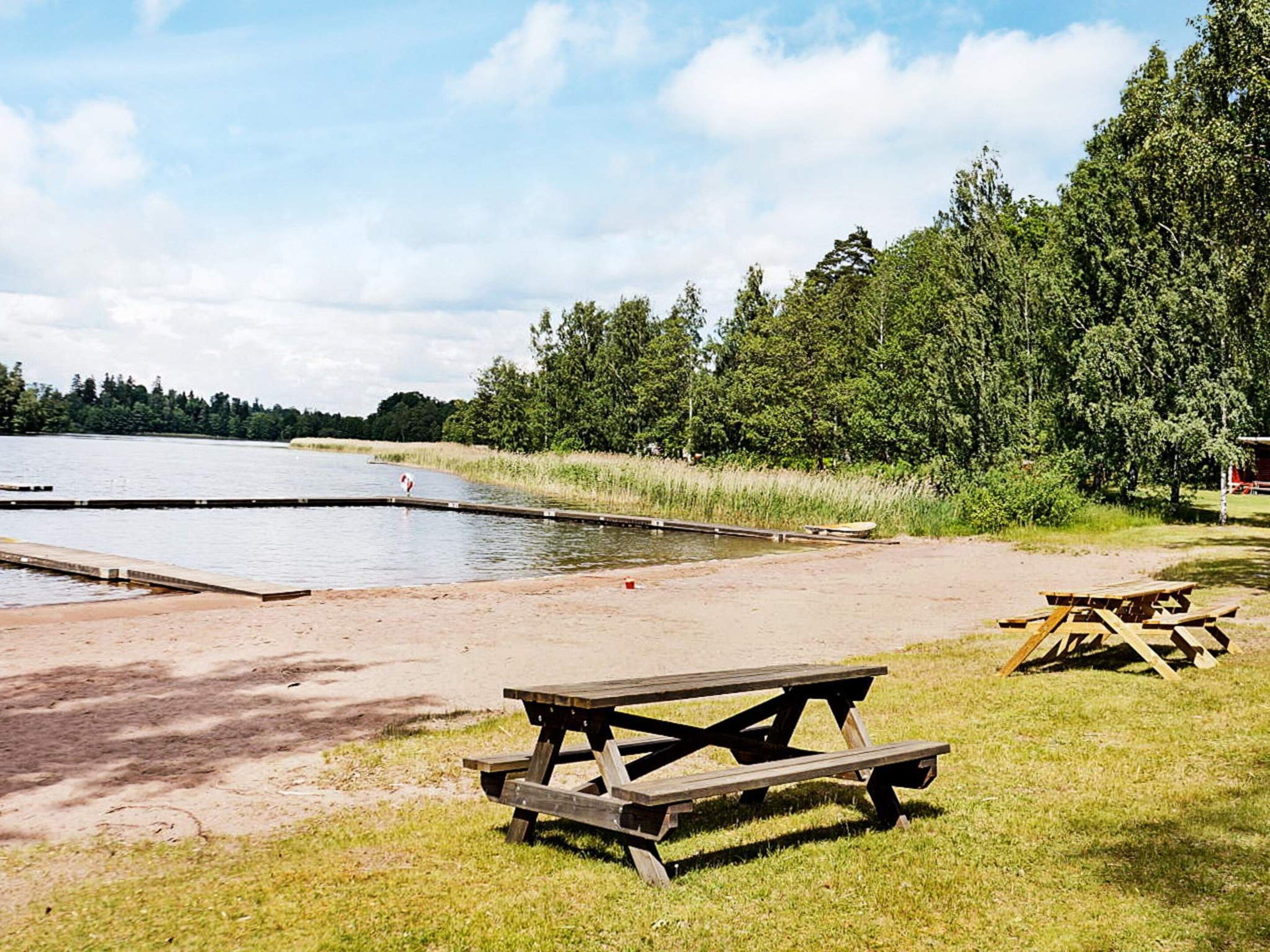 Un área de picnic junto al lago con un banco y mesa de madera, rodeada de árboles y un cielo despejado.