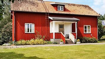 A red wooden house with a tiled roof, a small porch, and a visible window.