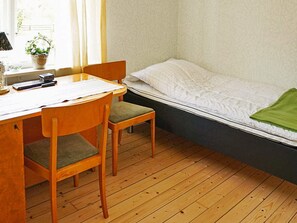 A small room with a wooden desk, a chair, a bed with a white mattress and green blanket, and a window with curtains. - 6 Person Holiday Home in Odensvi (Gamleby)
