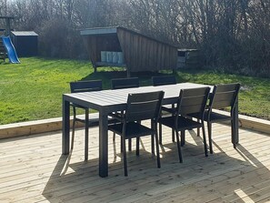 Une terrasse avec une table et des chaises, entourée d’une pelouse et agrémentée d’une aire de jeux.
