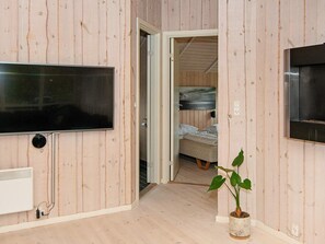 Une pièce aux murs recouverts de bois, un téléviseur à écran plat fixé au mur, un lit avec un matelas et des oreillers, et une plante en pot posée sur le sol.