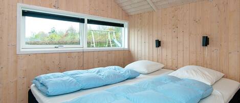 A bedroom with a bed, two windows, and wooden walls.