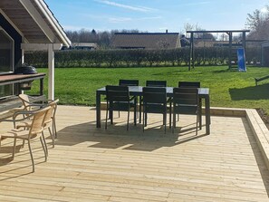 A covered outdoor patio with a table and chairs, a grill, and a playground in the background. - 4 Star Holiday Home in Sydals (Sydals)