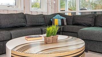 Ein modernes Wohnzimmer mit einem Ecksofa, einem runden Couchtisch mit Streifenmuster und einer Topfpflanze.