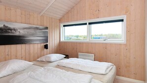 Quarto com paredes de madeira, uma janela grande, duas camas, um radiador e um quadro.