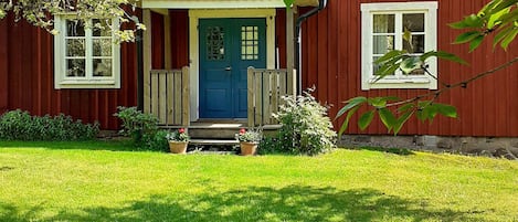 A red building with a blue door, a front porch, and a small garden.
