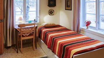 Una camera piccola e accogliente con un letto, una scrivania con una sedia, una sveglia e una finestra con tende.