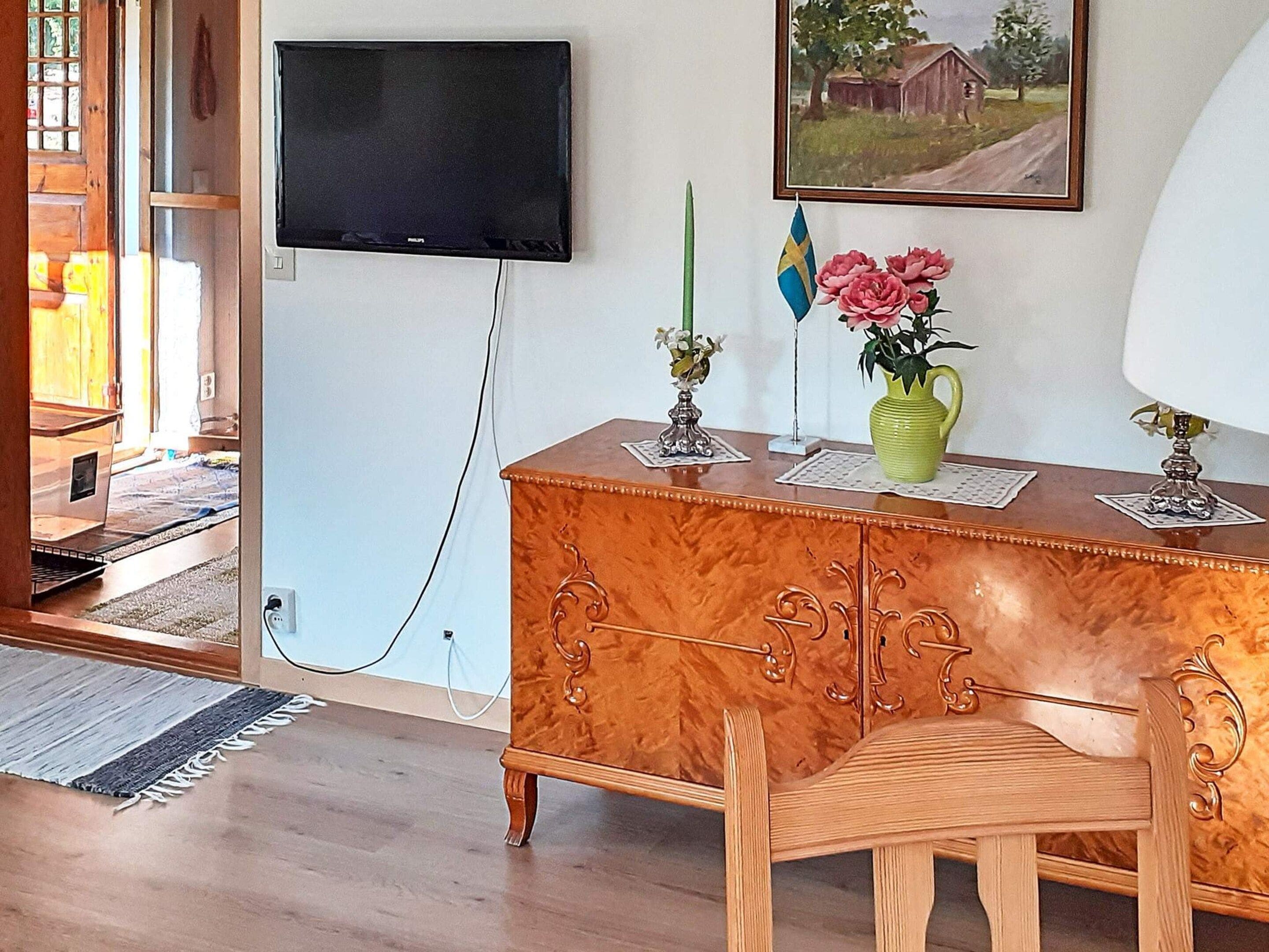 A room with a wooden cabinet, a television mounted on the wall, a painting, and a flag.