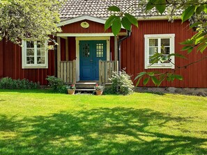 A red wooden house with a blue door, a front porch, and a small garden. - 6 Person Holiday Home in Alsterbro (Alsterbro)