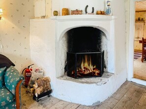 A fireplace with a fire, a wall with floral wallpaper, and a chair with a patterned cover. - 4 Person Holiday Home in Skruv (Skruv)