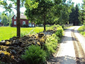 A rural road with a stone wall, green vegetation, and a red house in the background. - 4 Person Holiday Home in Skruv (Skruv)